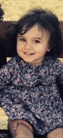 a little girl wearing a blue and pink floral dress smiles for the camera