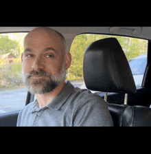 a bald man with a beard is sitting in the back seat of a car