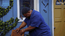 a man in a blue shirt is working on a chair in front of a blue house with a bet logo on the door