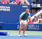 a man holding a tennis racquet on a tennis court in front of a wall that says hotels & resorts