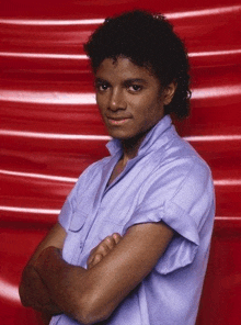 a young man in a blue shirt stands with his arms crossed in front of a red background