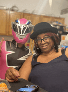 a woman wearing glasses sits next to a girl wearing a pink power ranger mask