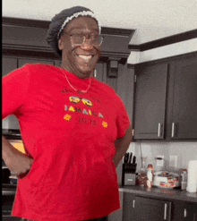 a woman wearing a red jamaica t-shirt is smiling in a kitchen