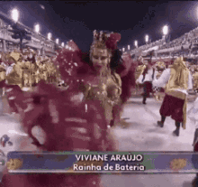 a woman in a red dress is dancing in front of a crowd with the name viviane araujo on the bottom right