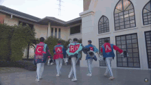 a group of cheerleaders are walking in front of a building with the letter c on the back of their jackets