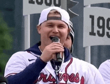 a man in a baseball uniform is holding a microphone in his hand and singing into it .