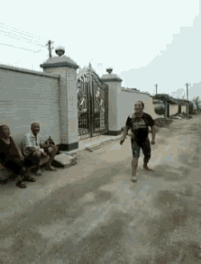 a group of people are sitting on a bench on the side of a dirt road while a man is running down the road .