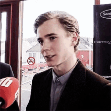 a young man in a suit is talking into a microphone in front of a sign that says no smoking