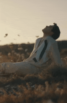 a man is sitting in a field with his arms outstretched and looking up .