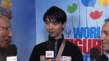 a man is talking into a microphone while standing in front of a sign that says world figure skating .