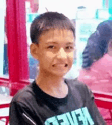 a young boy is sitting at a table in a restaurant wearing a black t-shirt .