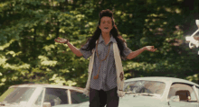 a woman with her arms outstretched is standing in front of two cars