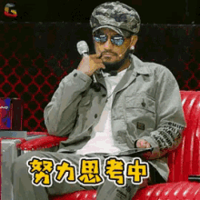 a man wearing sunglasses and a hat is sitting on a red couch holding a microphone ..