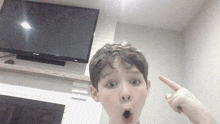 a young boy is pointing up at something in front of a flat screen tv