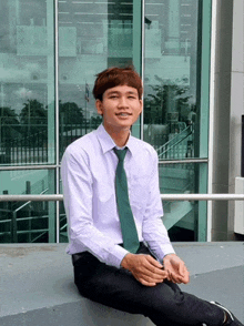 a man wearing a white shirt and green tie is sitting on a wall