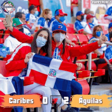 two women wearing face masks are sitting in a stadium with a score of caribes 0 to 2