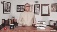 a man stands at a desk with a stack of books and a blue mug that says he 's up of nothing