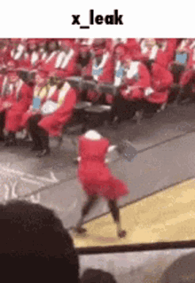 a girl in a red dress is dancing in front of a crowd of people at a graduation ceremony .