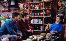 a group of people are sitting around a table with a merry christmas banner hanging on a shelf behind them