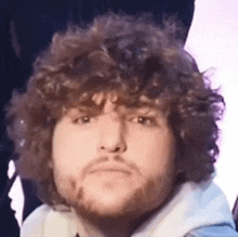 a young man with curly hair and a beard is making a funny face .