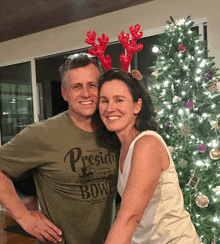 a man and woman are posing in front of a christmas tree wearing reindeer antlers