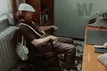 a man is sitting in a chair in front of a typewriter in a room with the letter w on the wall .