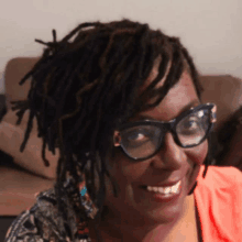 a woman with dreadlocks is wearing glasses and smiling