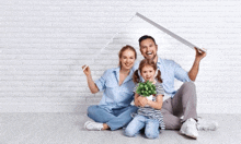 a family is sitting on the floor in front of a white brick wall holding a white roof .