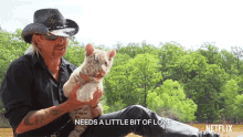 a man in a cowboy hat holds a small white tiger cub and says needs a little bit of love