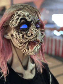 a woman with pink hair is wearing a mask that looks like a monster