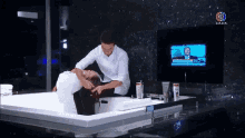 a man is washing another man 's hair in a bathtub in front of a tv that says 3