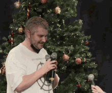 a man holding a microphone in front of a christmas tree wearing a shirt that says ' gun reform ' on it