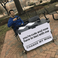 a man in a blue shirt sits at a table with a sign that says change my mind