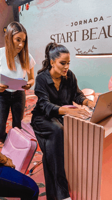 a woman is sitting at a desk with a laptop in front of a sign that says start beauty