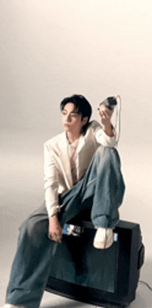 a young man is sitting on top of a television holding a telephone .