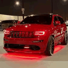 a red jeep grand cherokee is parked in a parking lot at night with red lights on it .