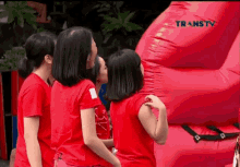 a group of girls in red shirts are standing in front of a large red balloon with transtv written on it