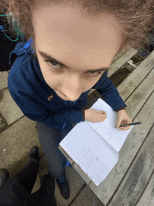 a girl wearing a blue jacket with the letter fn on it is writing in a notebook