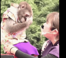 a woman is holding a monkey who is wearing a shirt and a purple skirt .