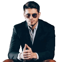 a man in a suit and sunglasses is sitting in a chair with his hands folded