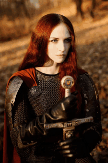 a woman with long red hair is holding a sword in her hands