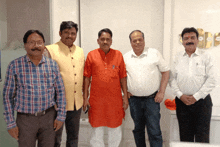 four men are posing for a picture and one of them is wearing a red kurta