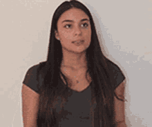 a young woman with long hair is standing in front of a white wall and looking at the camera .