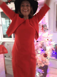 a woman in a red dress stands in front of a christmas tree