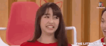 a woman wearing a red shirt and cat ears is making a funny face .