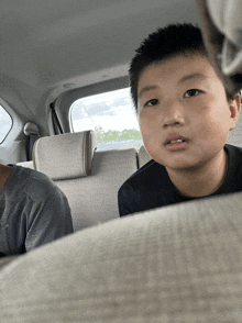 a young boy sits in the back seat of a car looking at the camera