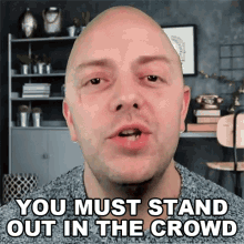 a bald man says " you must stand out in the crowd " in a room