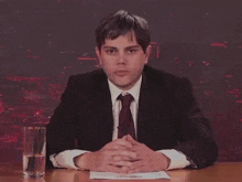 a man in a suit and tie sitting at a desk with his hands folded