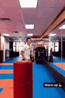 a man in a white shirt is standing next to a red punching bag in a gym with the words warm up below him