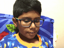 a young boy wearing glasses and a blue shirt with a dinosaur on it